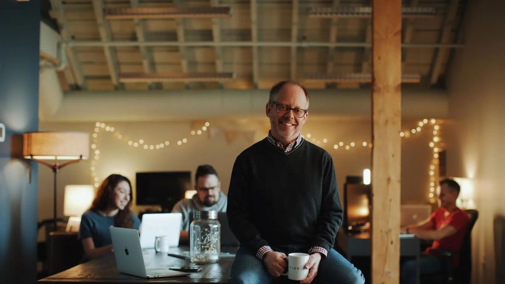 Man sitting on desk with others seated in the background